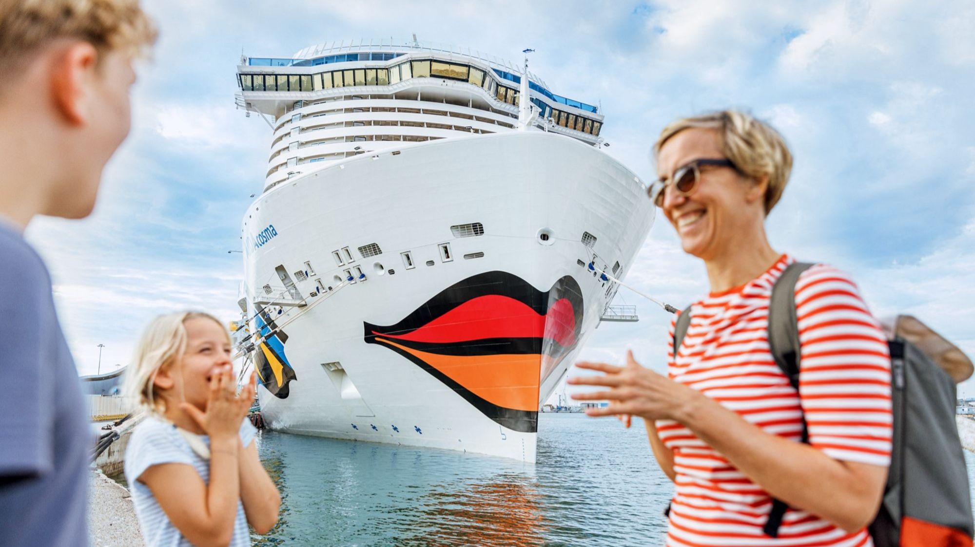 Mutter mit Tochter und Sohn lachend vor dem Kussmund der AIDAcosma | © AIDA Cruises