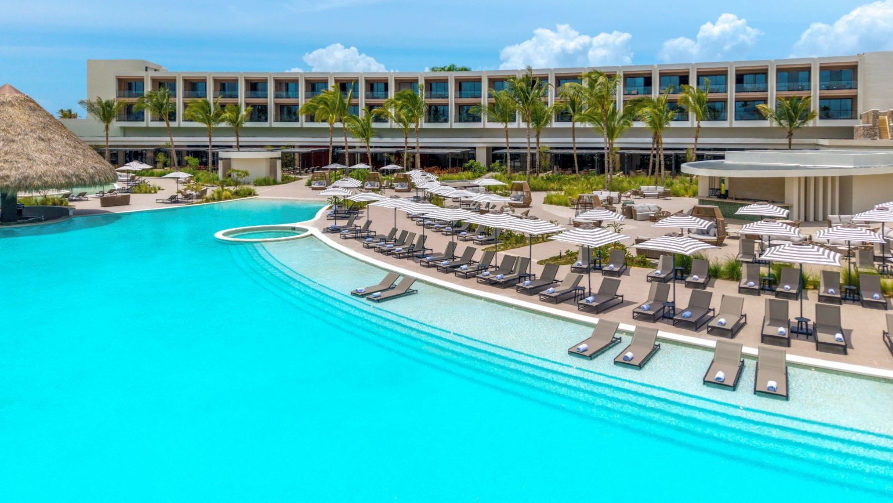 Luftaufnahme des Hauptpools im Zemi Miches Punta Cana Resort mit Liegestühlen, Sonnenschirmen und modernem Hotelgebäude im Hintergrund |  © 2025 Hilton
