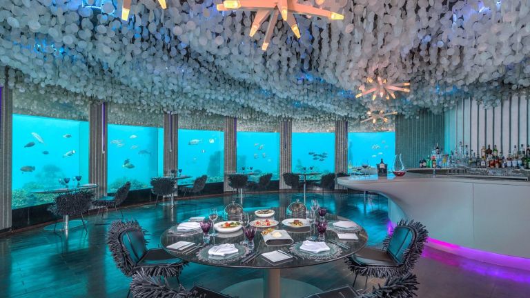 Elegantes Unterwasserrestaurant mit Blick auf Fische durch grosse Panoramafenster und stilvoll gedeckten Tischen |  ©  2025 Niyama Private Islands Maldives