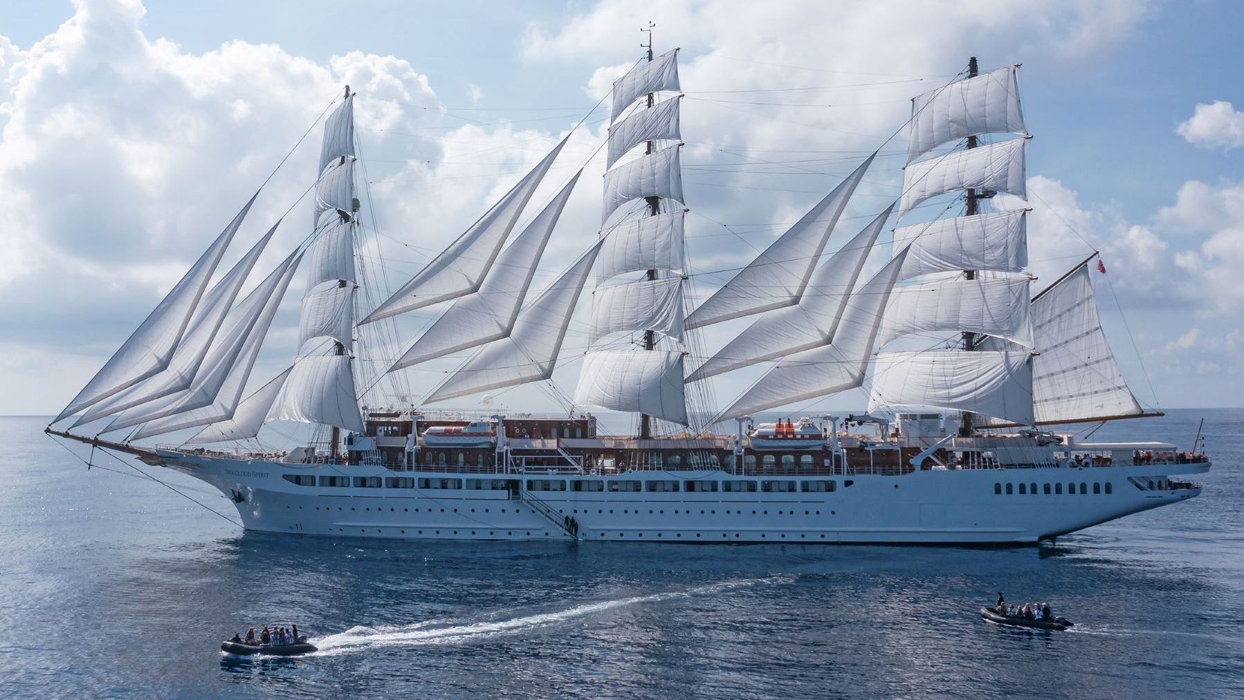 Grosses Segelschiff mit weissen Segeln auf ruhiger See, begleitet von zwei kleinen Motorbooten mit Passagieren | © SEA CLOUD CRUISES
