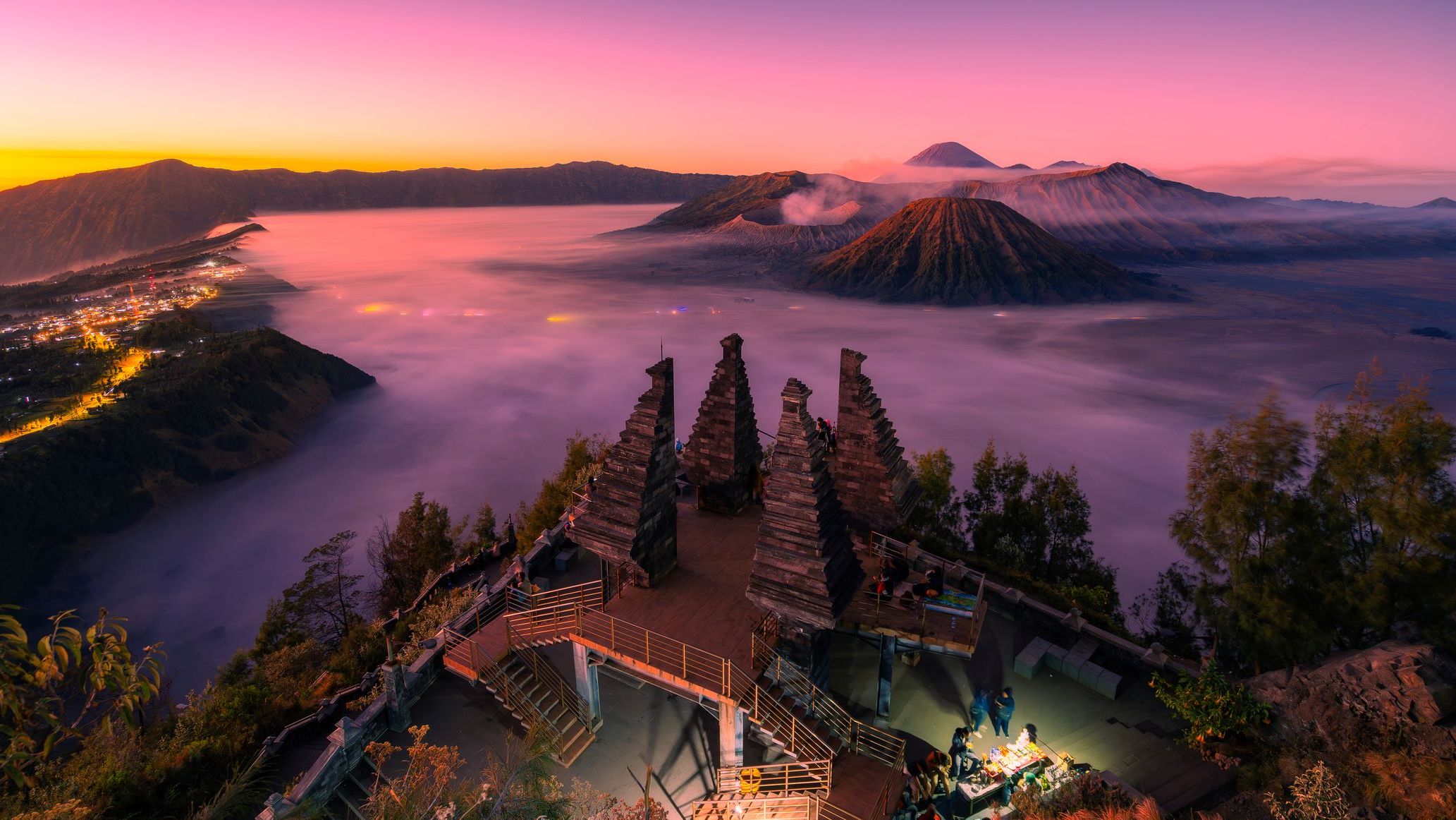 Aussichtsplattform Seruni Point mit traditionellen balinesischen Toren bei Sonnenaufgang, im Hintergrund der Vulkan Bromo und die Tengger-Caldera auf Java, Indonesien, umgeben von Nebel und farbig beleuchtetem Tal | © AdobeStock